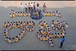 Students sit and perform in the shape of Rakhi