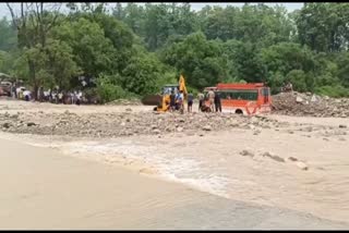 Rescue operation of a bus in Ramnagar Nainital  bus got stuck in the middle of Dhangarhi drain in Ramnagar Nainital  ഉത്തരാഖണ്ഡിൽ മഴ ശക്തം  കനാലിൽ കുടുങ്ങിയ ബസ് പുറത്തെടുത്തത് ജെസിബി ഉപയോഗിച്ച്  ഉത്തരാഖണ്ഡ് മഴ  നൈനിറ്റാൾ രാംനഗർ ധൻഗർഹി കനാൽ അപകടം  Dhangarhi Nala bus accident  ധൻഗർഹി നല ബസ് അപകടം