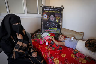 Palestinian mother Rasha Qadoom sits by her wounded child Rayed near a poster depicting her five-year-old daughter Alaa killed during the latest conflict between Israel and Palestinian militants, in Gaza on August 9, 2022. Alaa was the first of 16 children killed in three days of intense conflict between Israel and Islamic Jihad militants in the densely populated Palestinian enclave of Gaza. (Photo by Mahmud HAMS / AFP)
