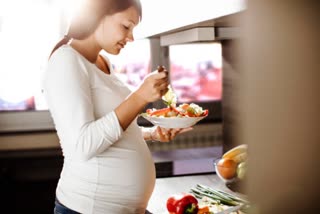 An pregnant woman eating healthy food in the kitchen .