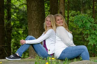 Slim and overweight woman sitting back to back at forest edge