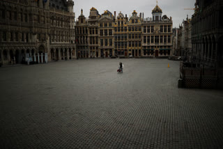 In this Friday, March 20, 2020 file photo, a man riding a bicycle takes photographs in a virtually empty Grand Place in Brussels.