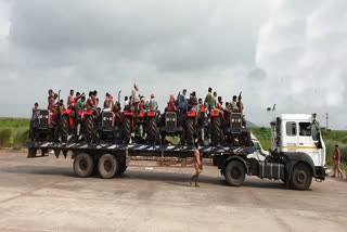 Migrant workers travel on trailer truck laden with tractors to reach home