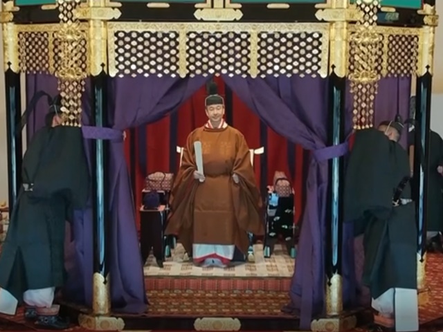 The emperor wears a voluminous robe and a hat topped with a towering black tail