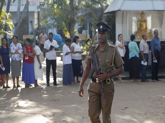 Sri Lankans queue to cast their votes as a police officer secures at a polling station