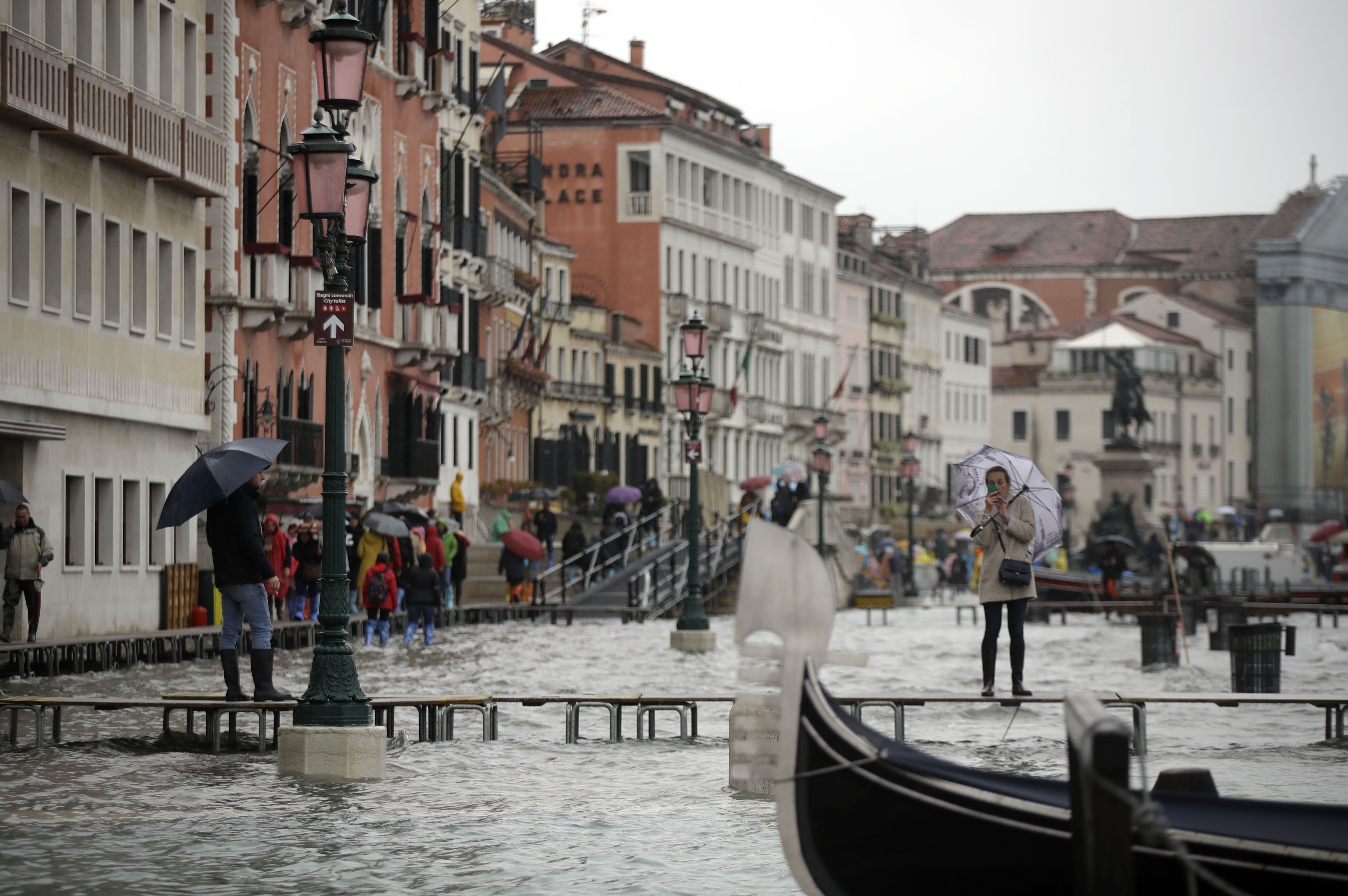 A woman standing on catwalk, right, set up on the occasion of a high tide takes pictures, in a flooded Venice, Italy.