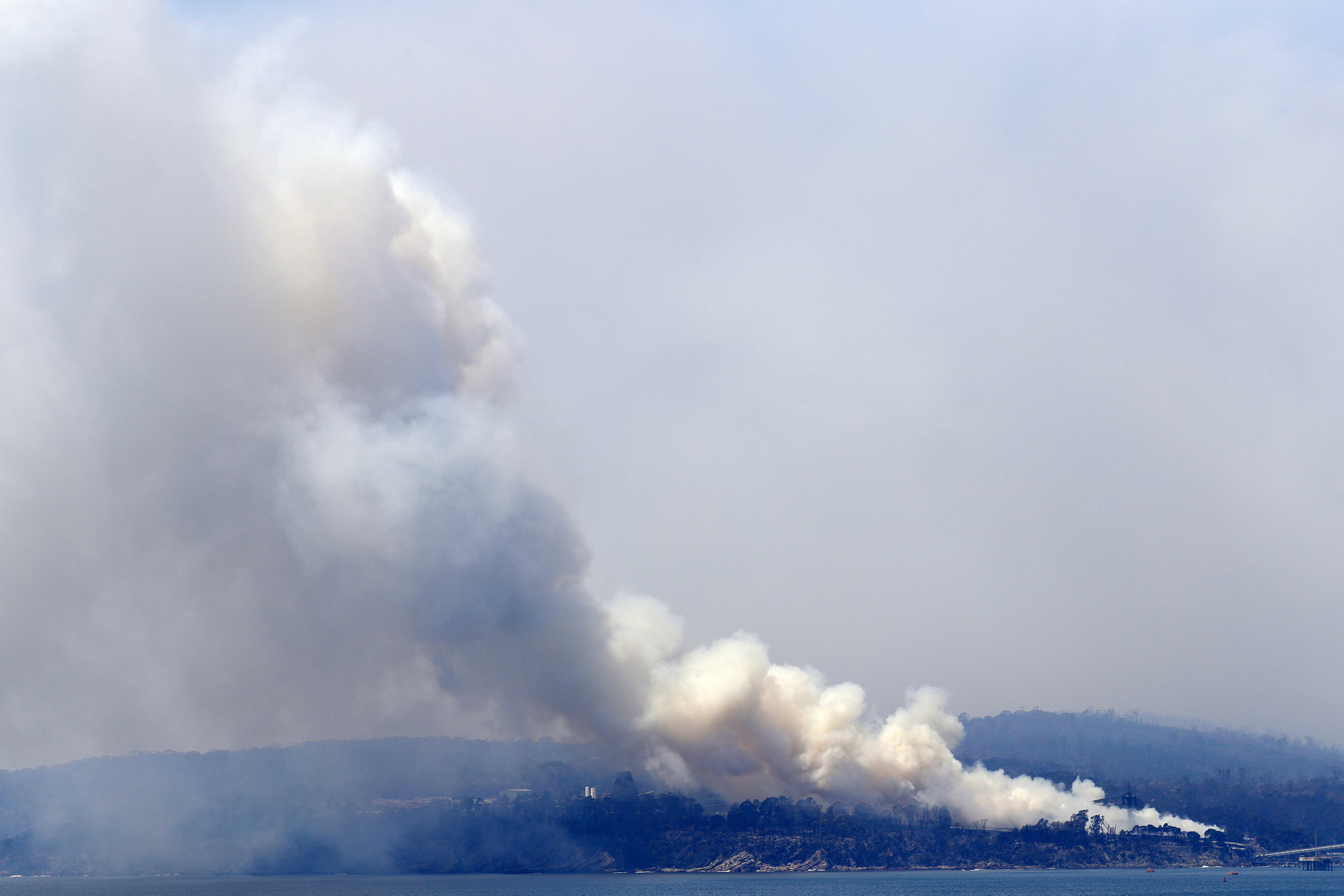 A plume of smoke rises from a fire in a huge wood chip pile at a mill in Eden, Australia, on Saturday after catching alight where nearby wildfires sparked the blaze.