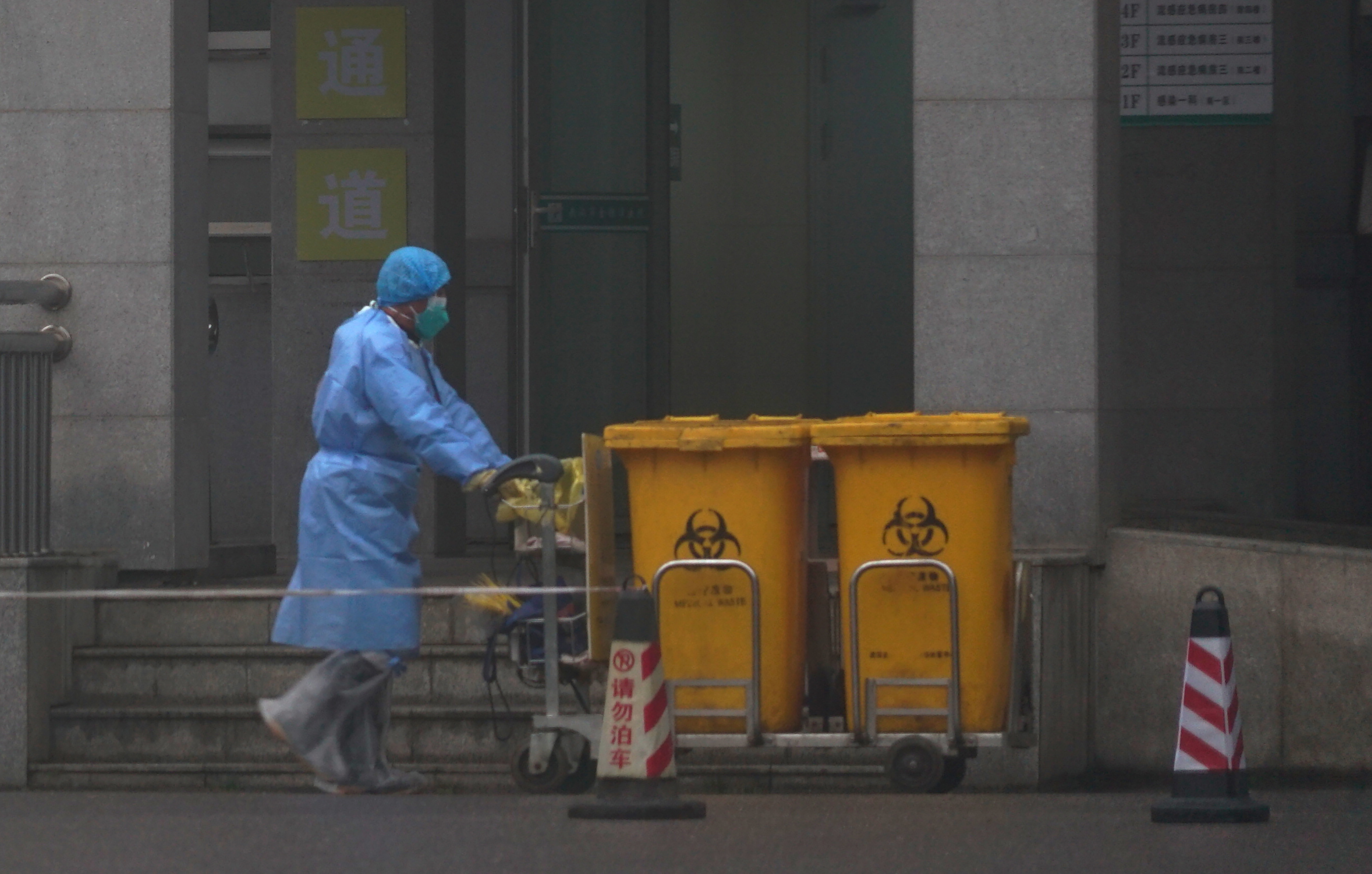 Staff move bio-waste containers past the entrance of the Wuhan Medical Treatment Center, where some infected with a new virus are being treated, in Wuhan, China