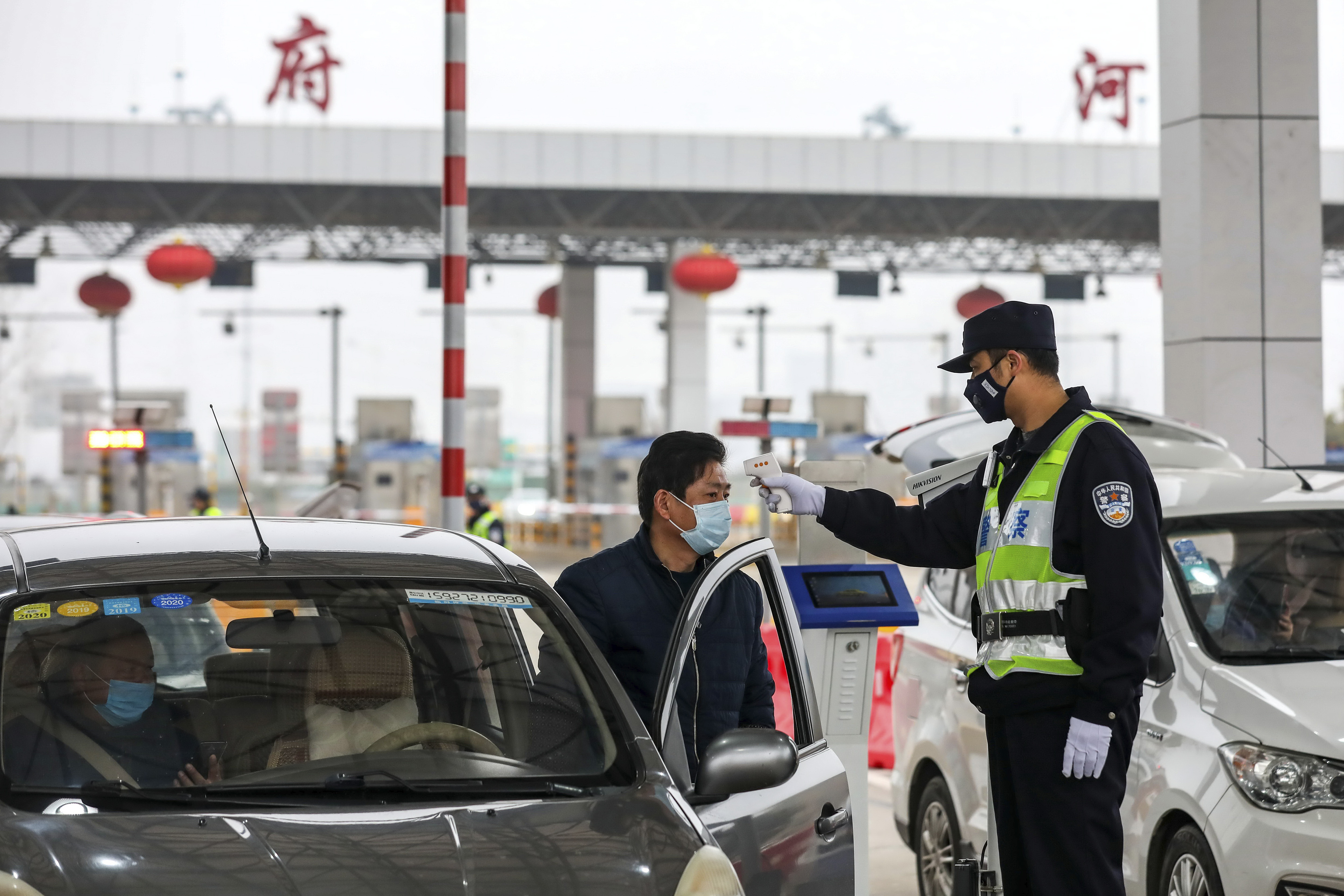 A policeman uses a digital thermometer to take a driver's temperature at a checkpoint at a highway toll gate in Wuhan in central China's Hubei Province