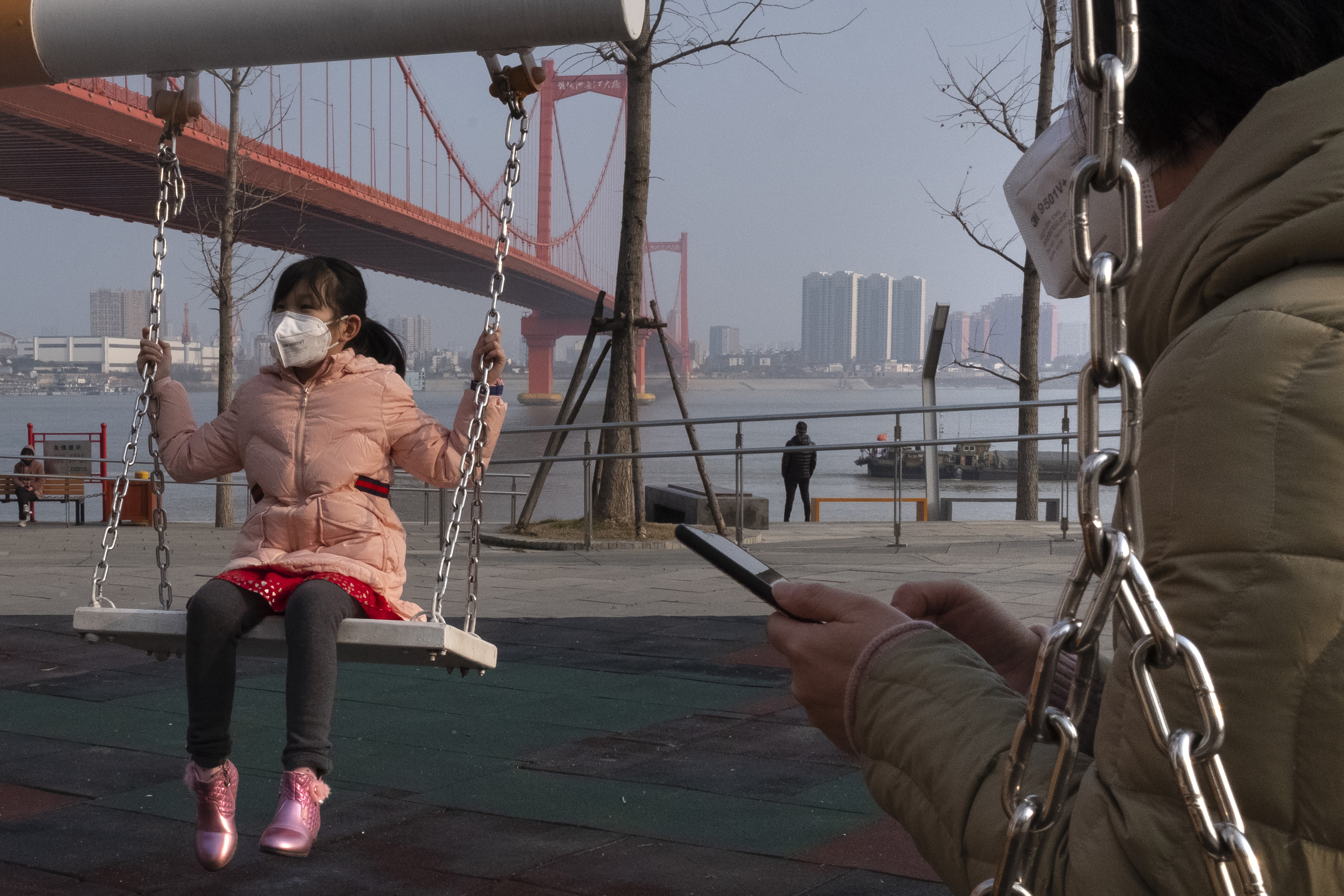 A girl wears a face mask as she play on a swing near the Yingwuzhou Yangtze River Bridge in Wuhan in central China's Hubei Province