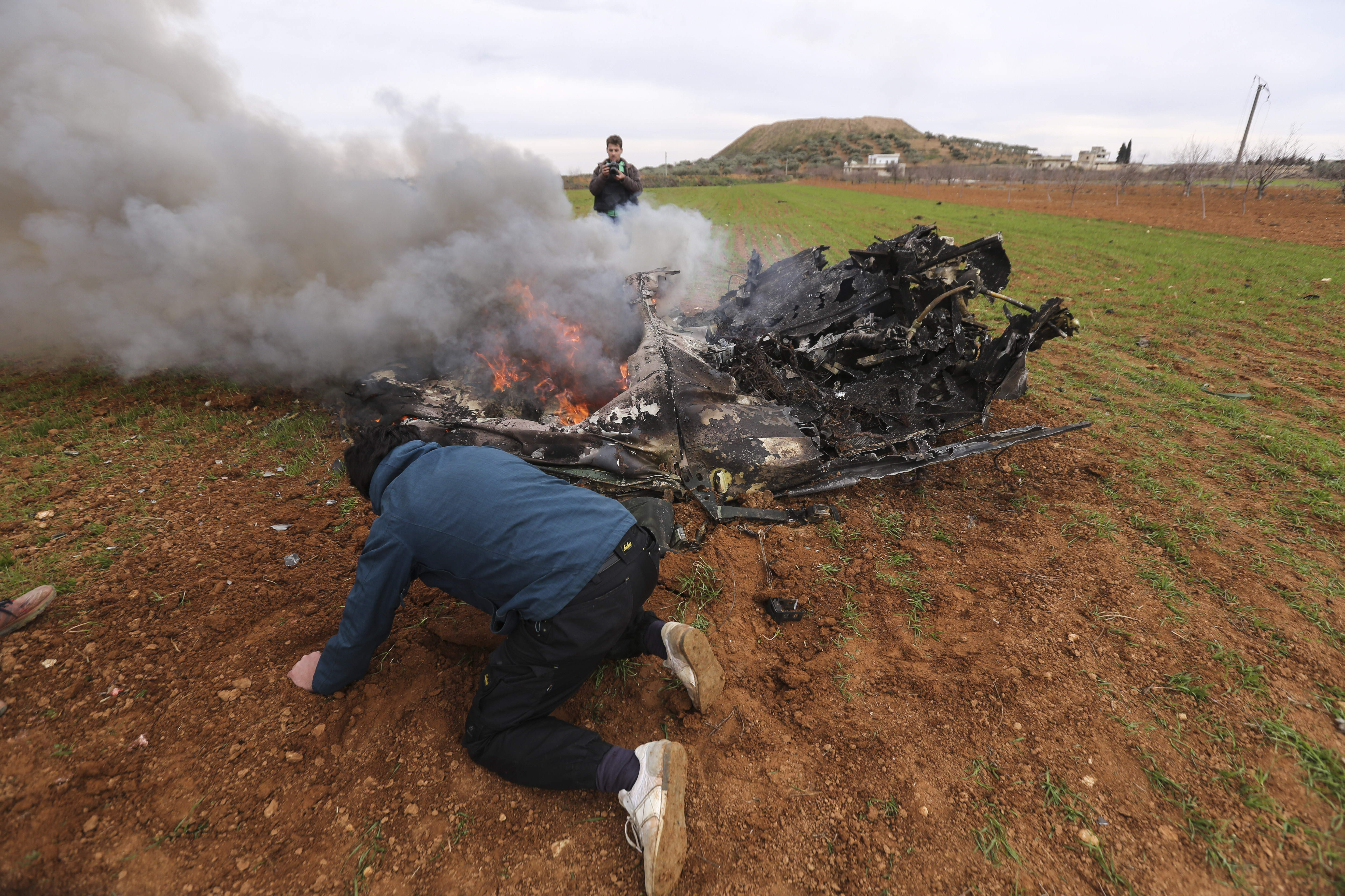 Rebel fighters look at a Syrian government helicopter that was shot down in Idlib province, Syria