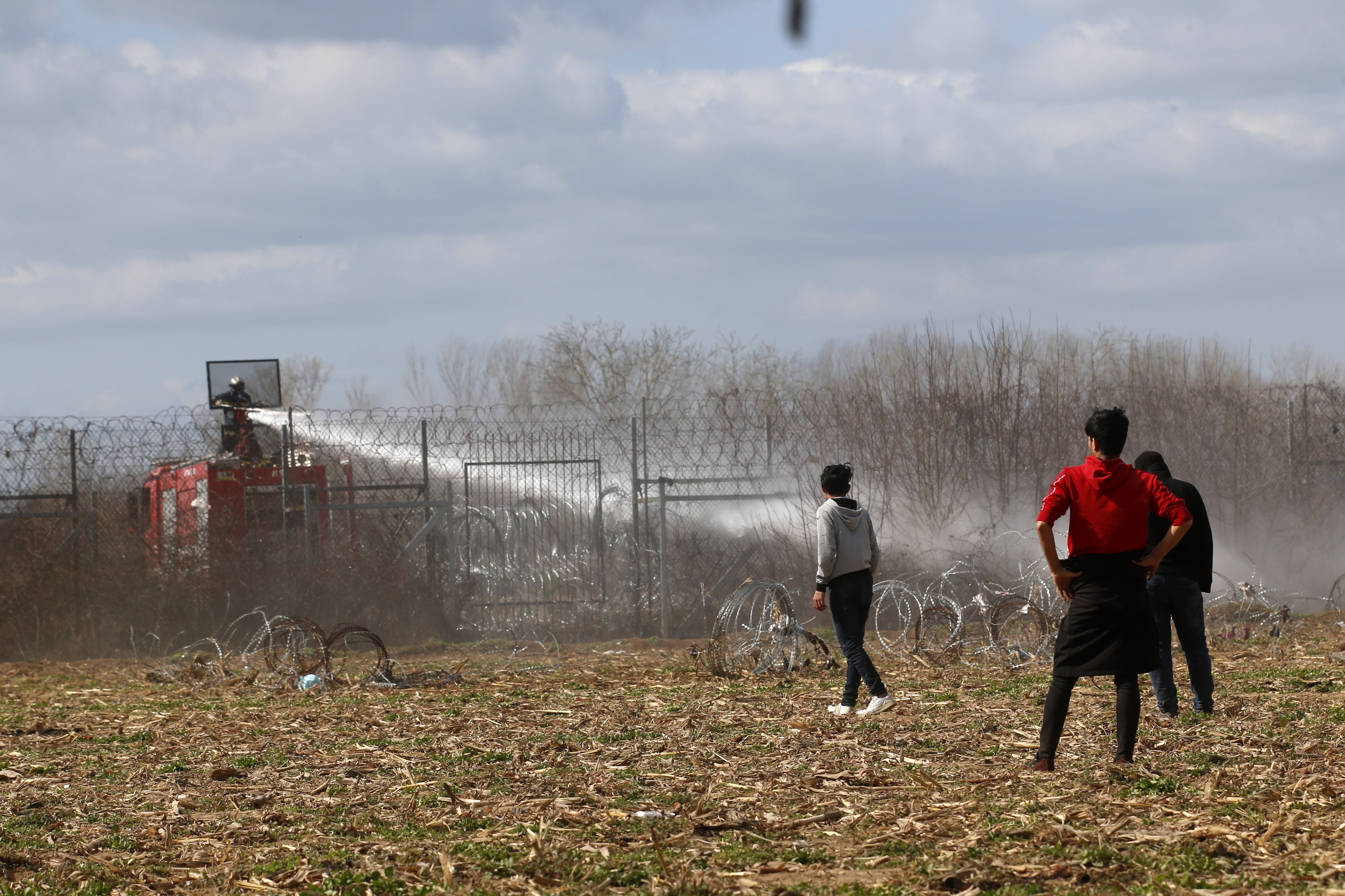 Greek firefighters spray water as migrants stand near a border fence on the Turkish side during clashes with the Greek riot police at the Turkish-Greek border in Pazarkule, Edirne region, on Saturday.