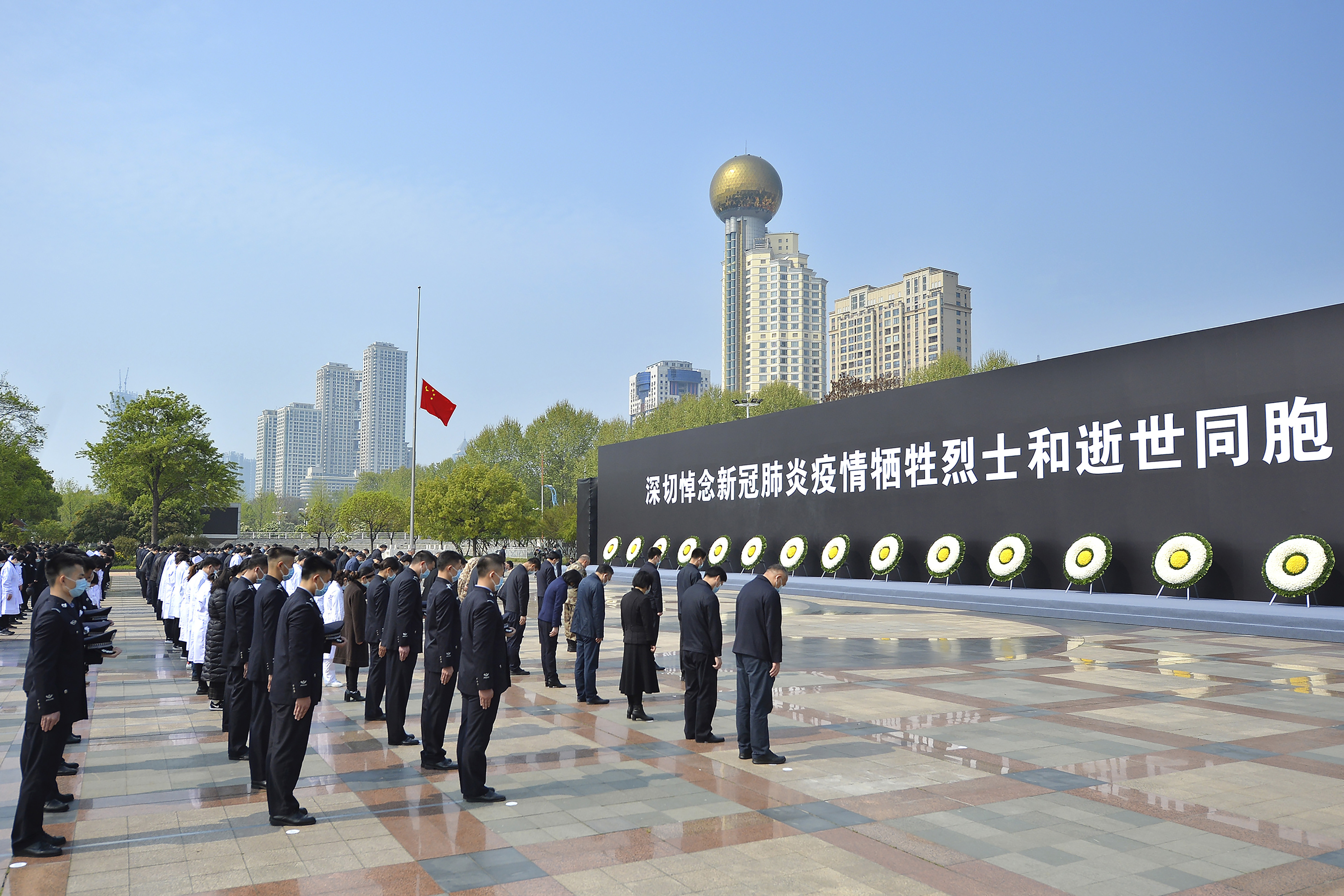 People bow their heads during a national moment of mourning for victims of coronavirus at an official ceremony in Wuhan in central China's Hubei Province