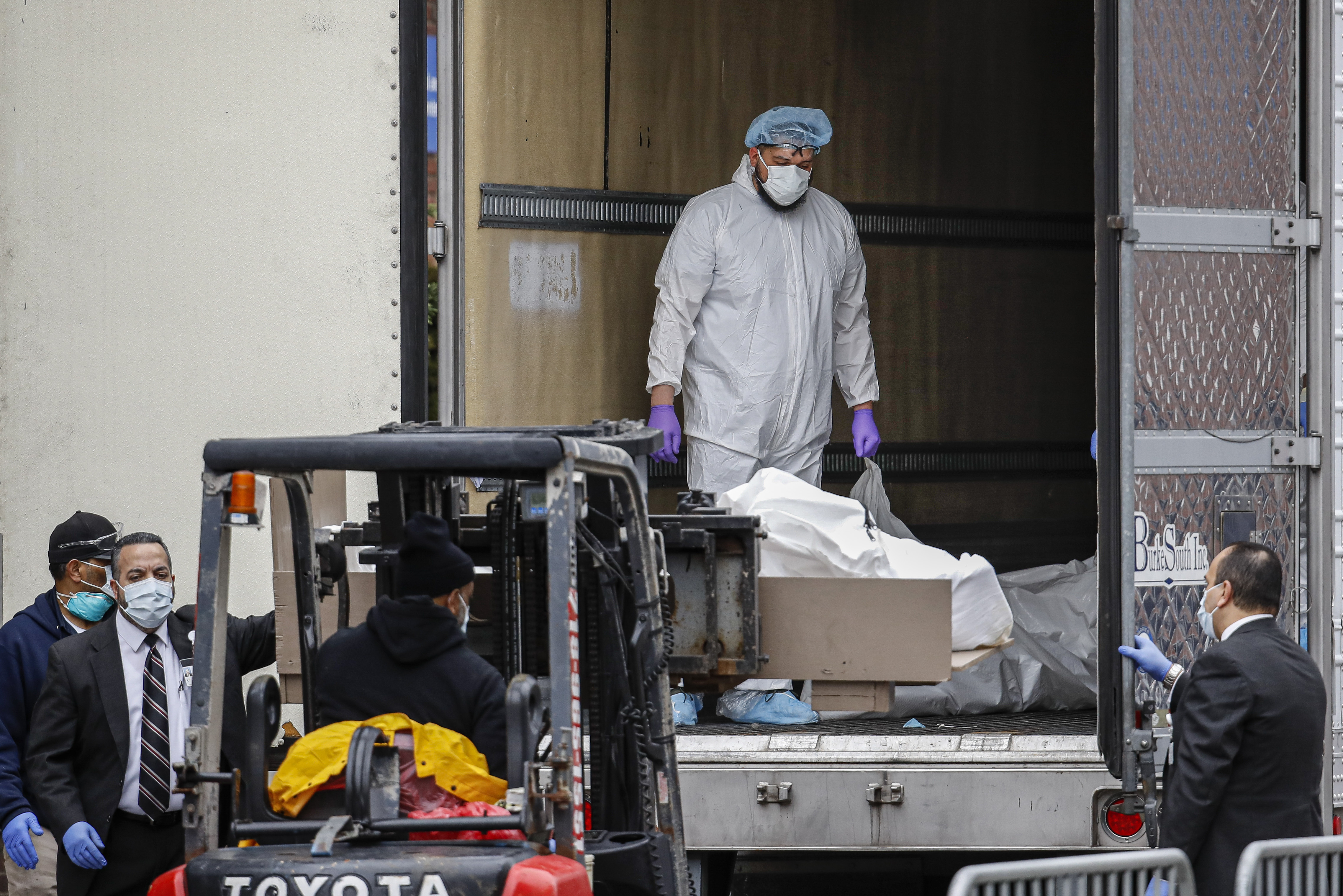 A body wrapped in plastic is loaded onto a refrigerated container truck used as a temporary morgue by medical workers wearing personal protective equipment due to COVID-19 concerns