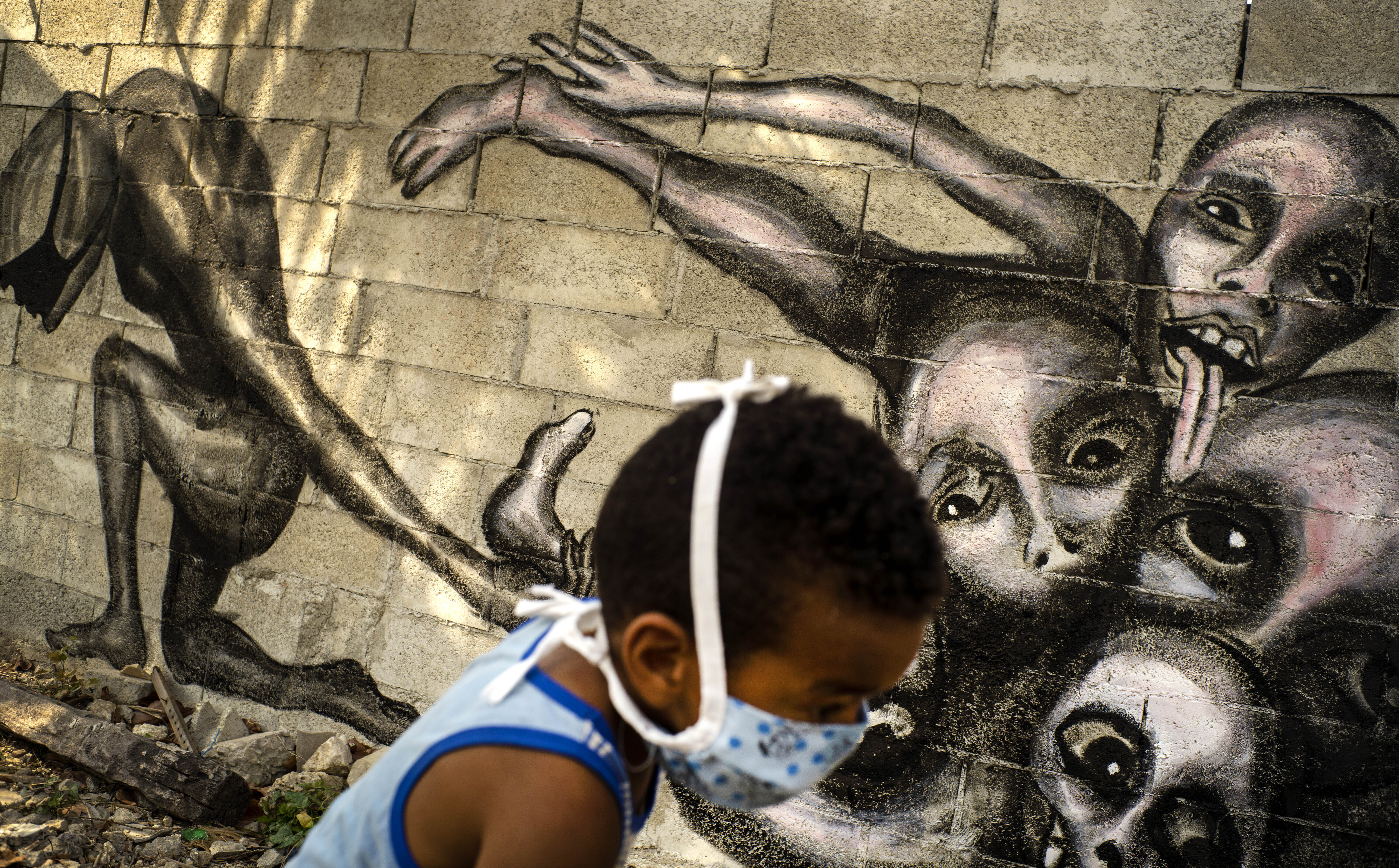 A boy wearing a mask as a precaution against the spread of the new coronavirus plays in front of a mural by artist Yuriel Pena titled 