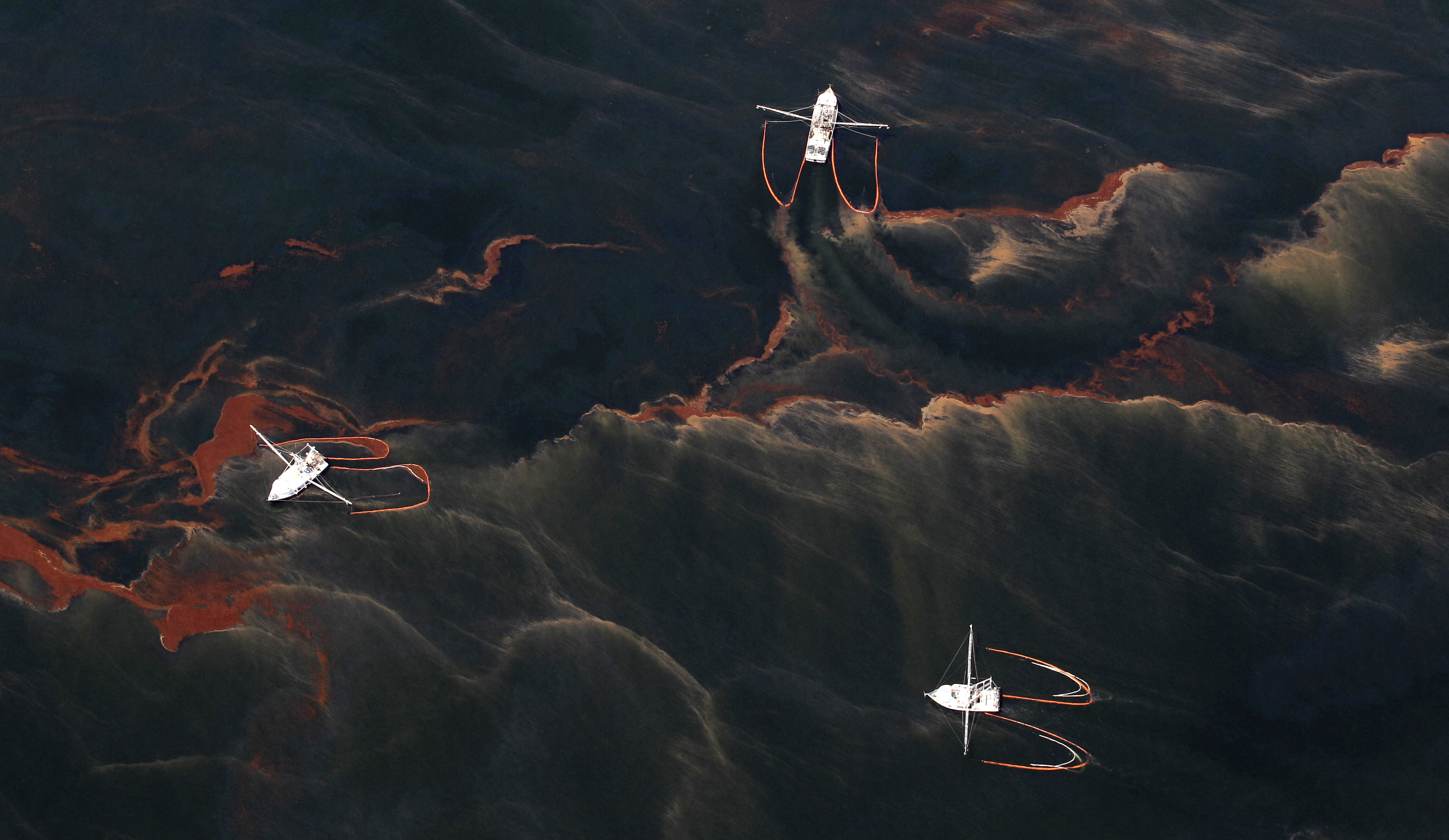 In this May 5, 2010 file photo, shrimp boats are used to collect oil with booms in the waters of Chandeleur Sound, La. Ten years after an oil rig explosion killed 11 workers and unleashed an environmental nightmare in the Gulf of Mexico, companies are drilling into deeper and deeper waters where the payoffs can be huge but the risks are greater than ever.