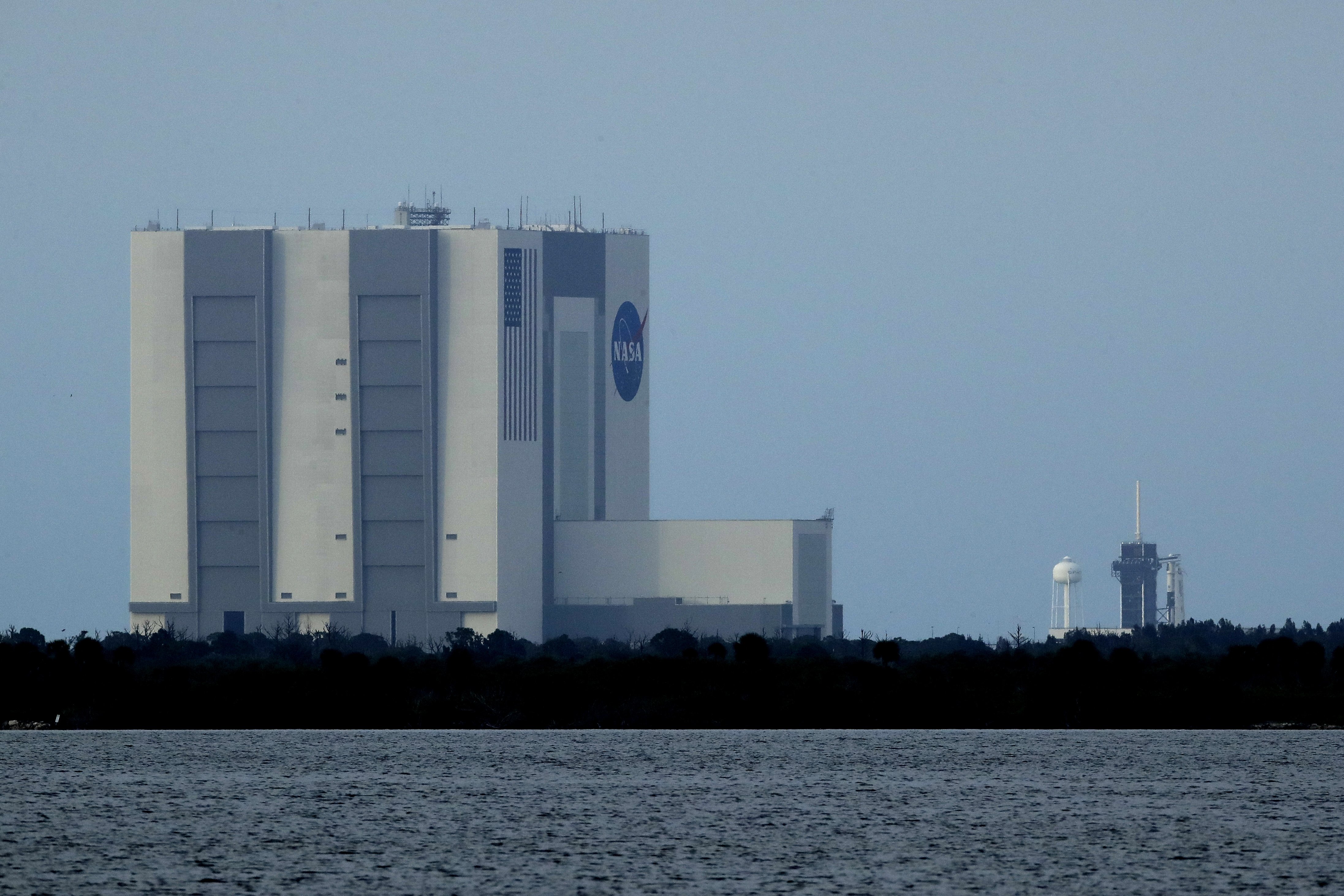 With the Vehicle Assembly Building pictured in the foreground, the SpaceX Falcon 9, with the Dragon capsule on top of the rocket, is seen on Launch Pad 39-A on Tuesday at Kennedy Space Center in Cape Canaveral.