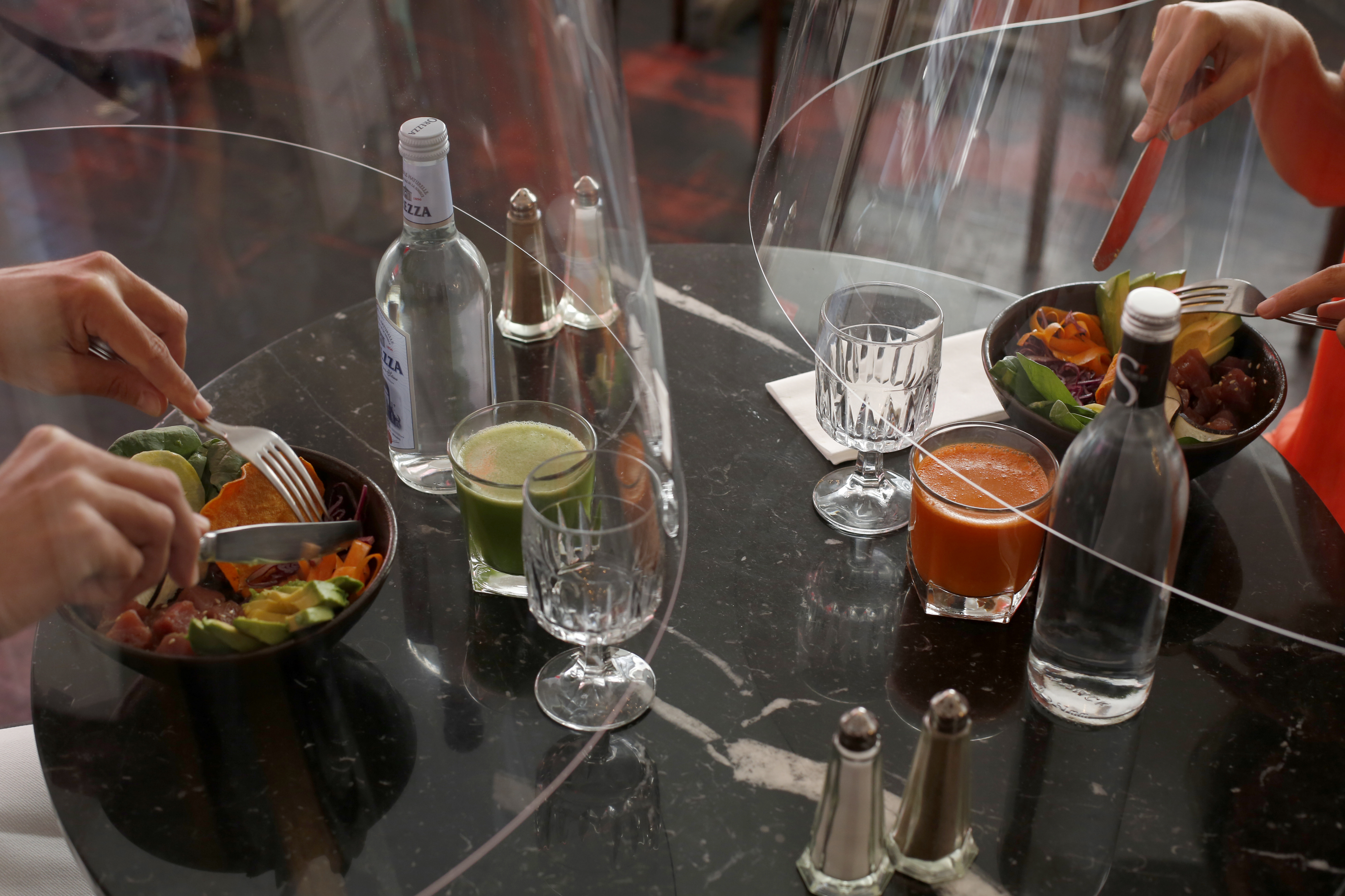 A man and a woman demonstrate dining under a plastic shield on Wednesday, in a restaurant of Paris.