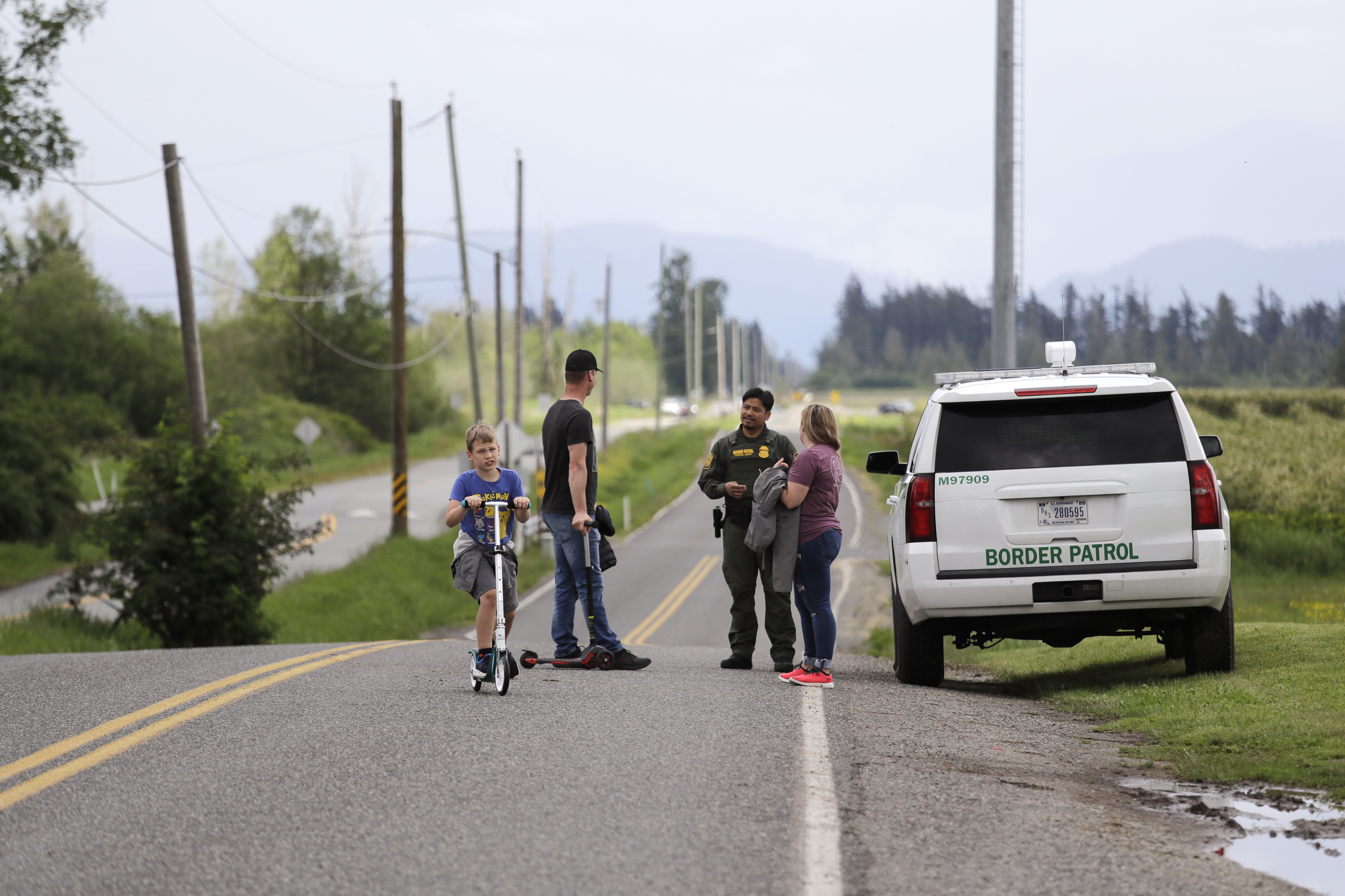 A Border Patrol officer in the U.S. talks with nearby residents on E. Boundary Rd., paralleling 0 Ave. behind them in Canada, near Lynden, Washington.
