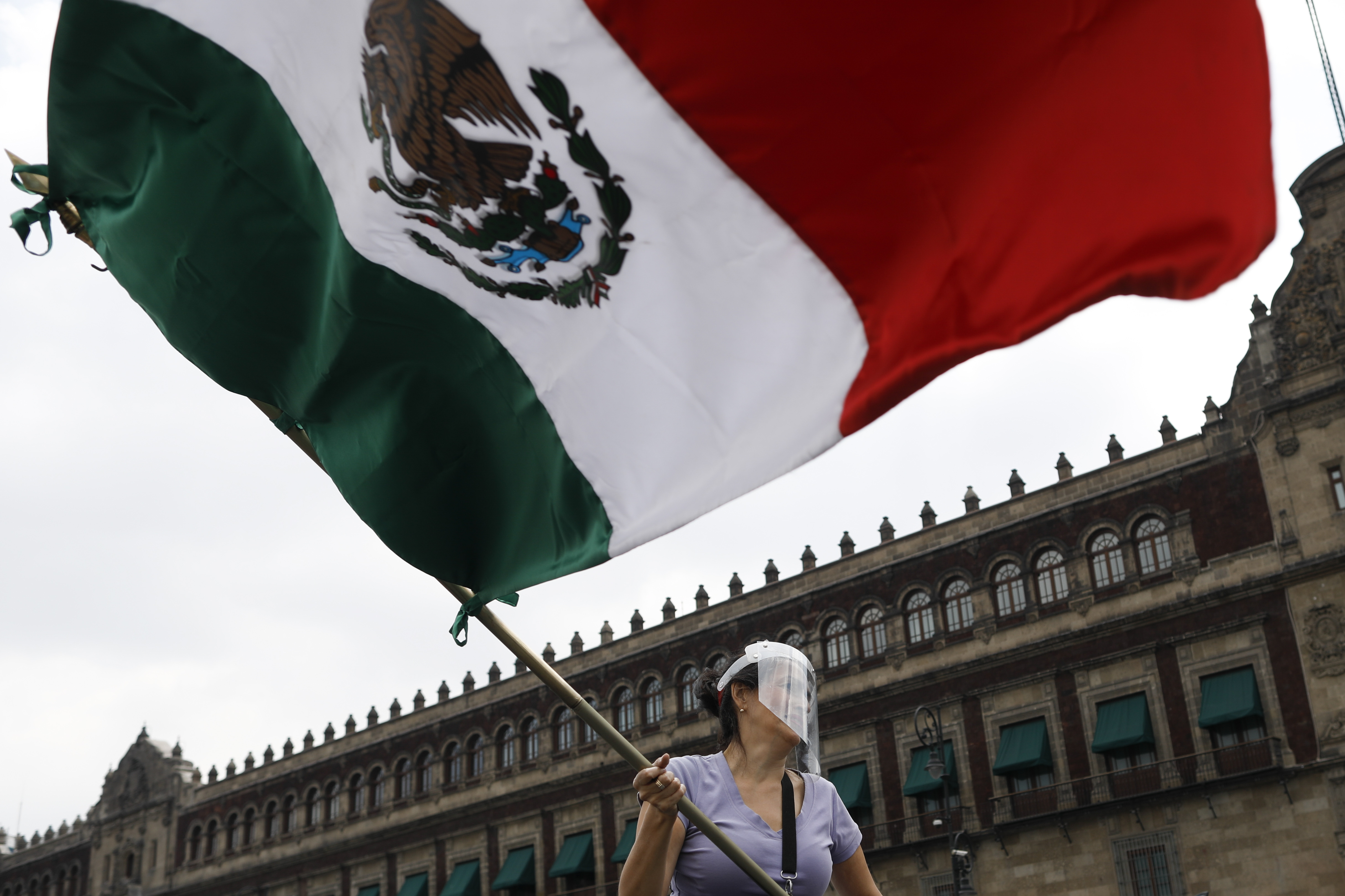 A woman wearing a face shield waves a Mexican flag in front of the National Palace during a caravan of cars protest calling for Mexican President Andres Manuel Lopez Obrador to step down, in Mexico City, on Saturday.