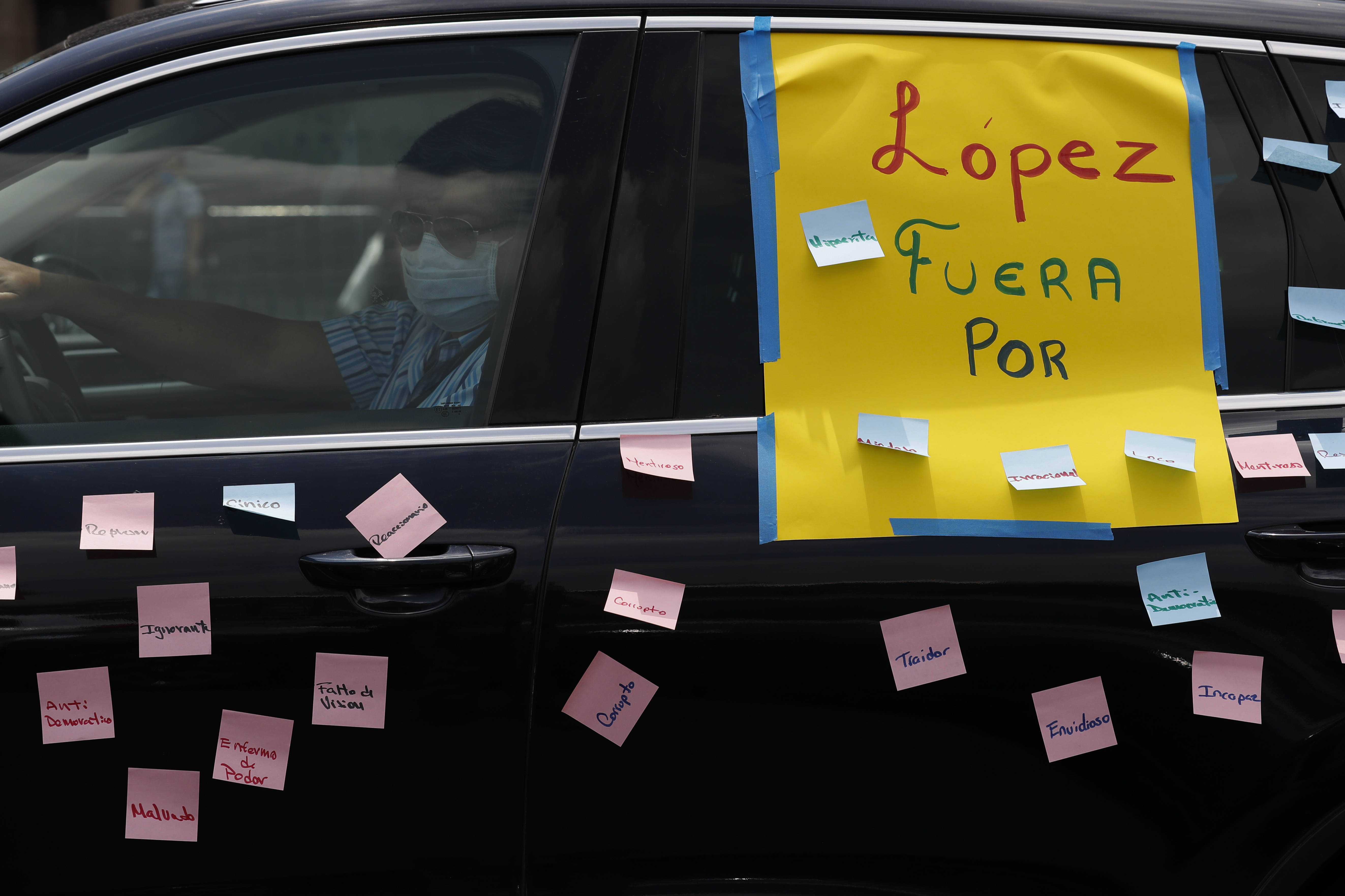 A man drives a car with a sign reading in Spanish; 