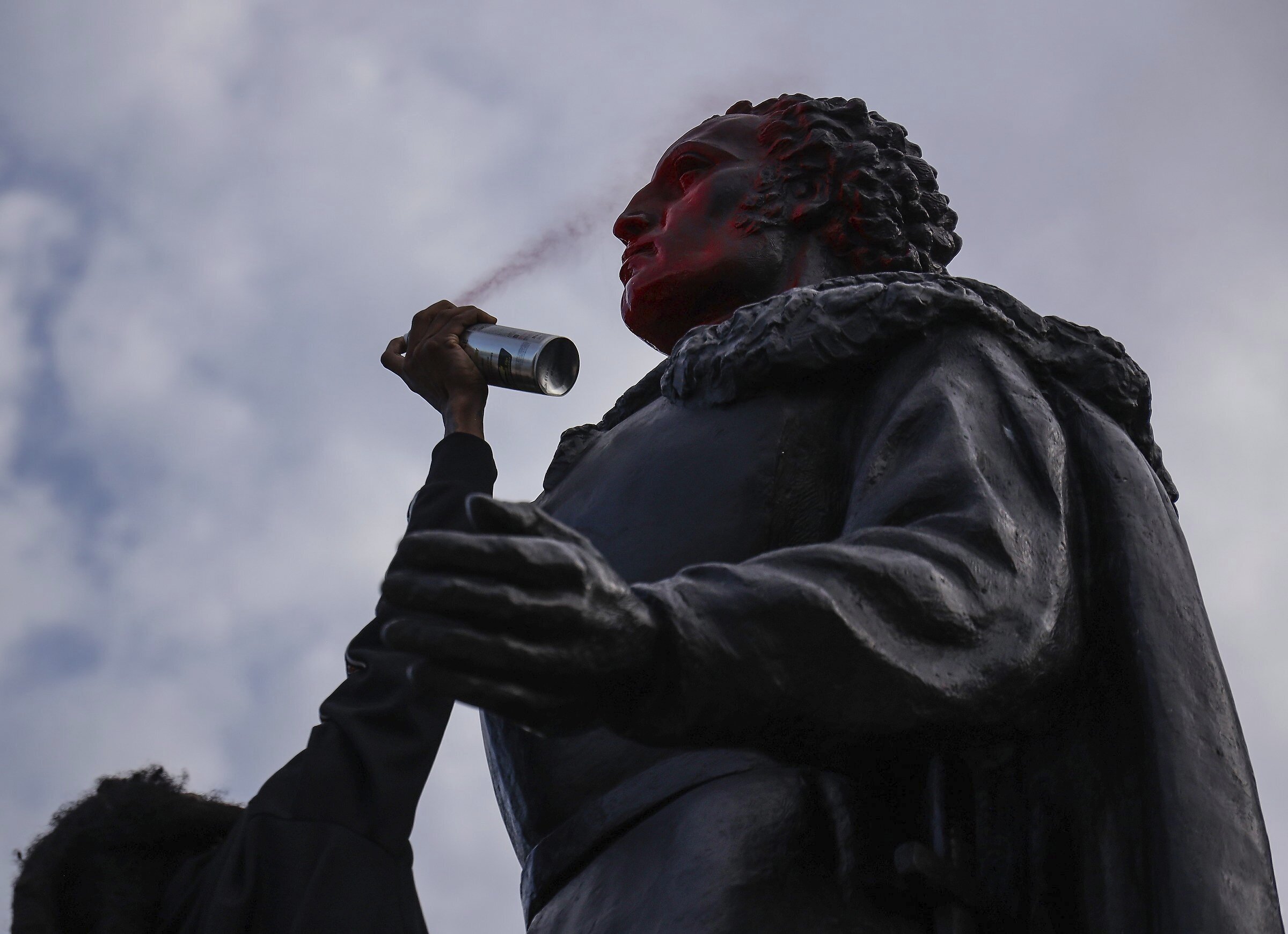 A protester spray paints the face of the statue of Christopher Columbus as the small group of protesters walked through Bayside in Miami and defaced bronze statue of Columbus and Ponce de Leon on Wednesday.