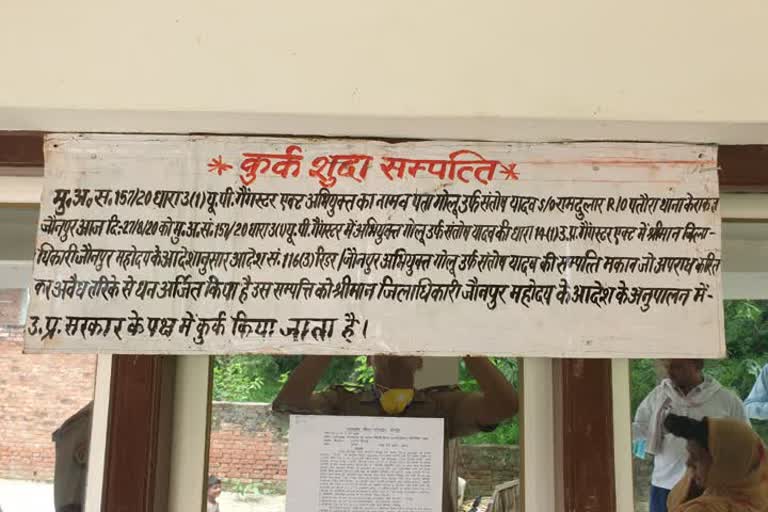 संपत्ति कुर्क करने के बाद पोस्टर लगाता पुलिसकर्मी