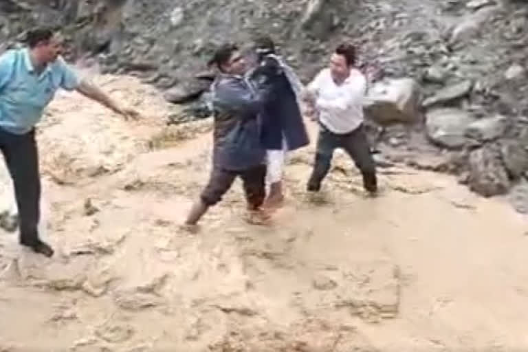 Teachers help students cross flooded stream