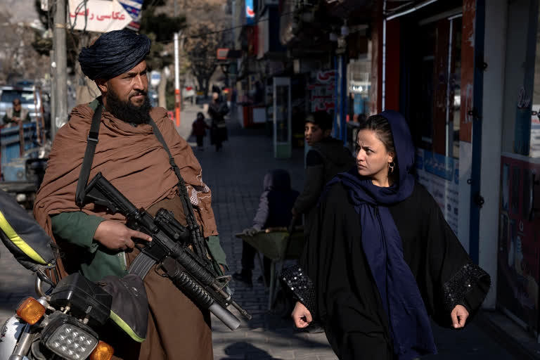 A Taliban fighter stands guard as a woman walks past in Kabul