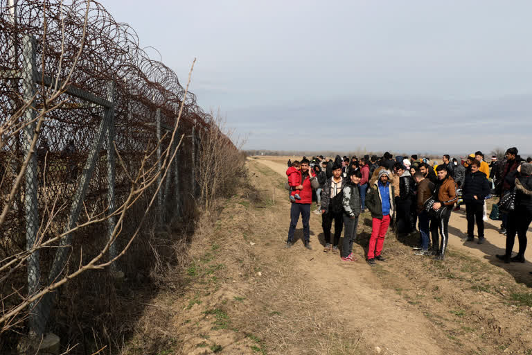 Greek border guards patrol, left, as migrants wait at he Turkey-Greece border in Pazarkule, Turkey, on Friday.