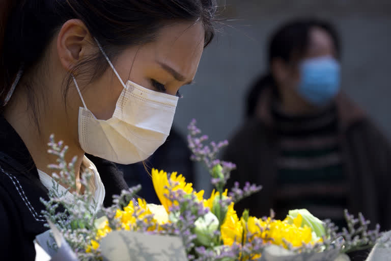 A woman holds a floral bouquet as people gather outside of a park where an official memorial was held for victims of coronavirus in Wuhan in central China's Hubei Province