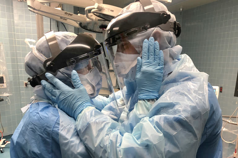 nurses Mindy Brock and Ben Cayer, wearing protective equipment, hold each other and look into each other's eyes, in Tampa General Hospital in Tampa, Fla.