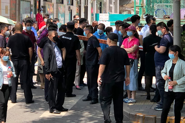 Police and security officials watch as people gather at a coronavirus testing center at a sports facility in Beijing