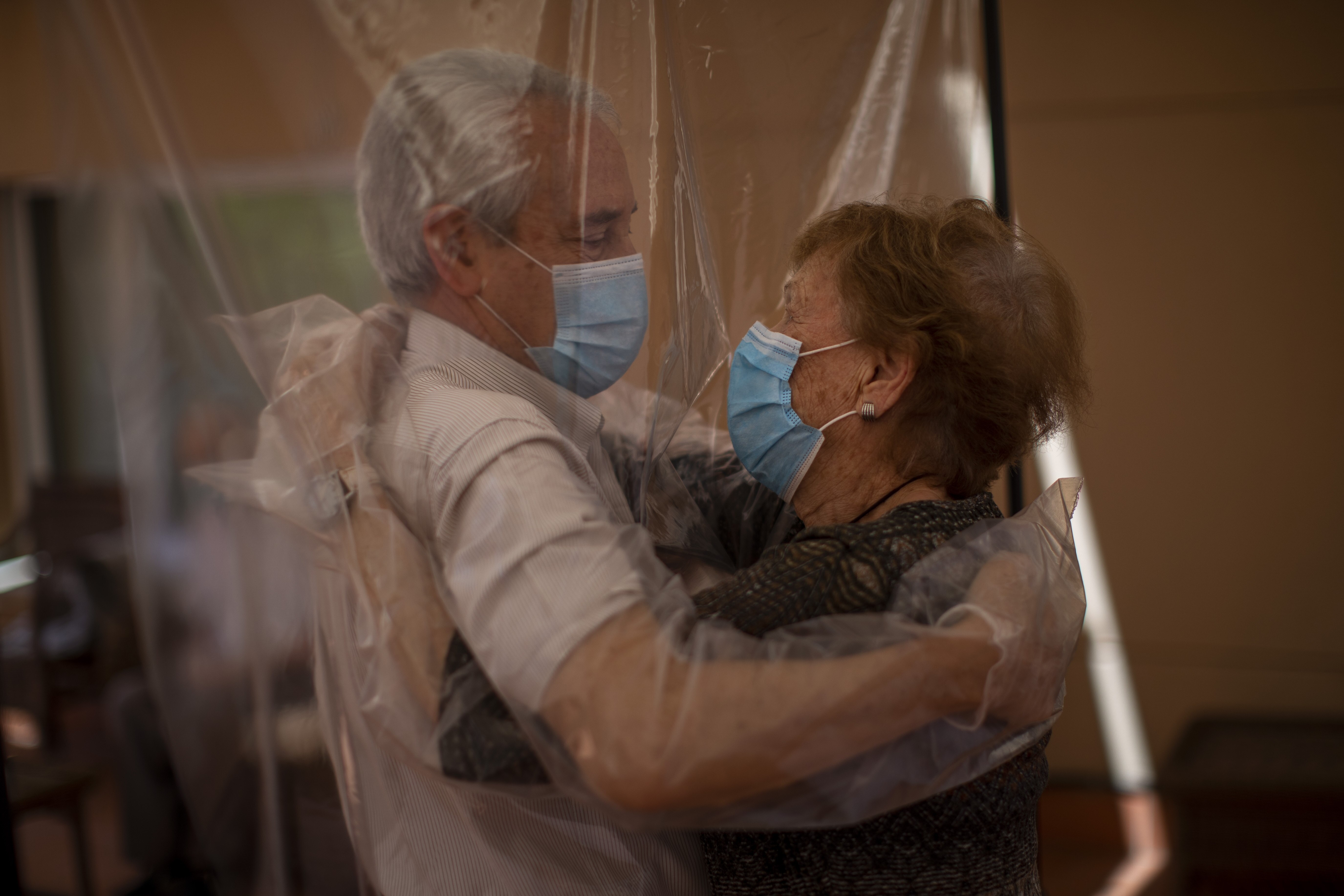 Isabel Pérez López receives an embrace through a plastic film screen from her visiting son-in-law Jose Maria Vila at a nursing home in Barcelona, Spain.