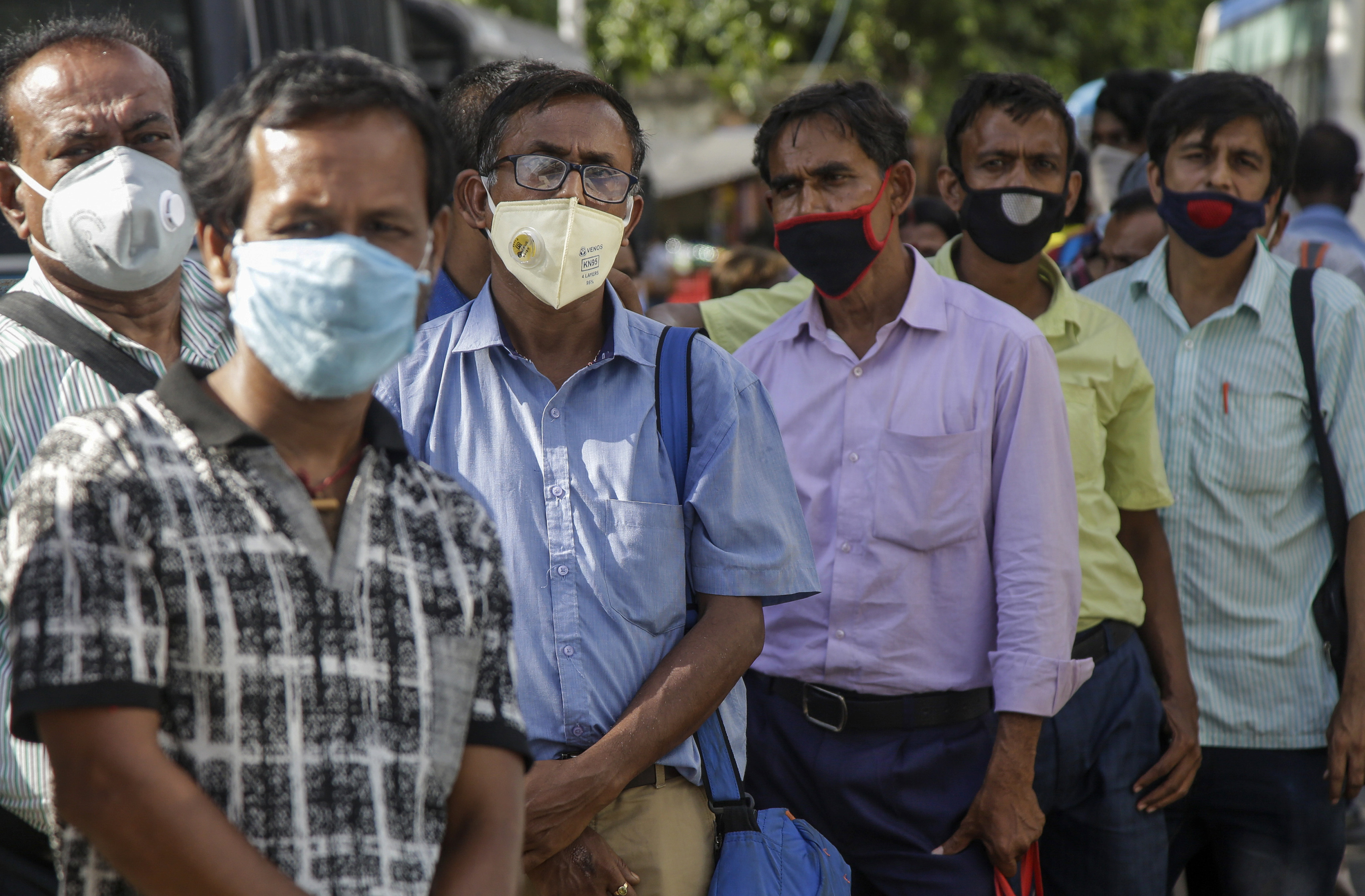 Commuters with face masks wait in a queue at a bus station in Kolkata, on Friday.