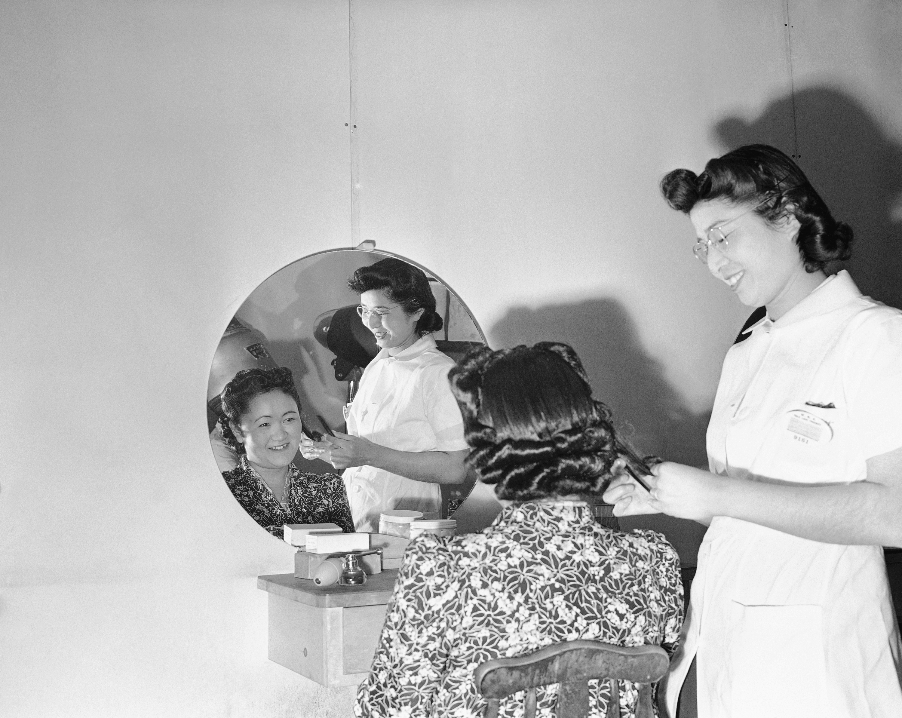 Mary Takita of Walnut Grove, Ca, works on the hair of Mrs. Y. Yoshihara of Olympia at the Japanese relocation camp in Tule Lake, Calif. (File)