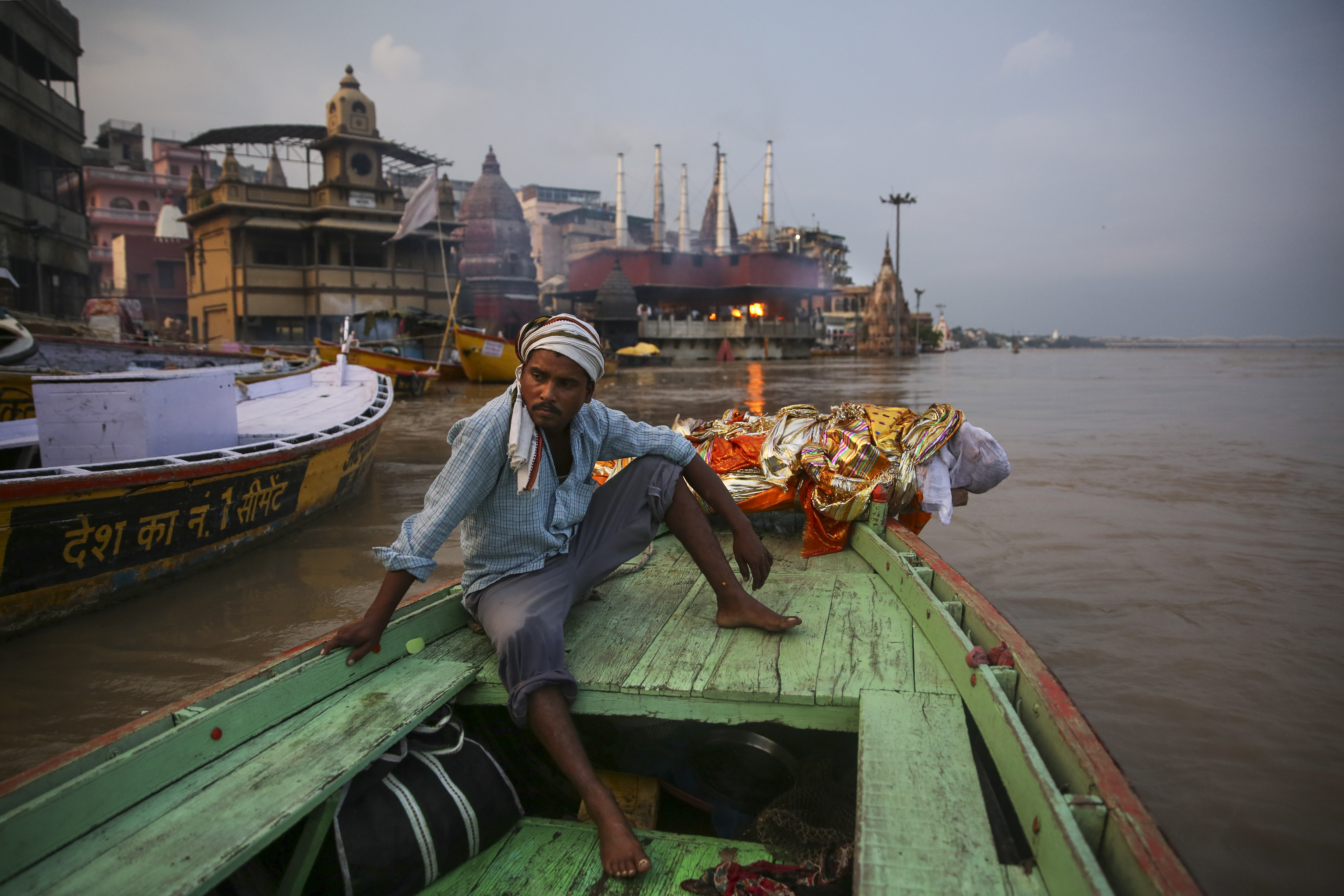 A worker who helps cremate bodies sits by the body of an elderly man, wrapped and weighed down by a large rock. For millions of Hindus, Varanasi is a place of pilgrimage and anyone who dies in the city or is cremated on its ghats is believed to attain salvation and freed from the cycle of birth and death.