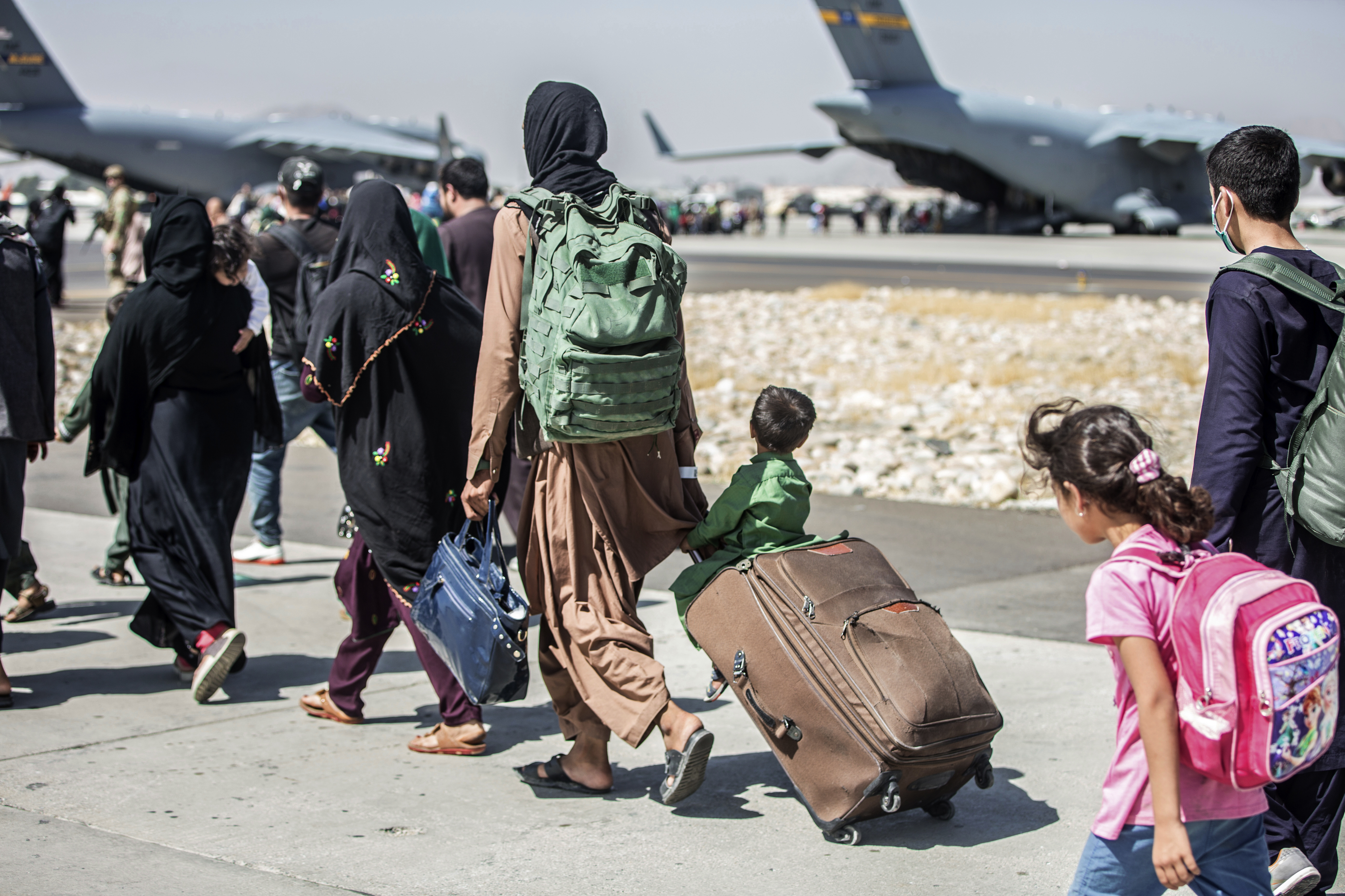 In this image provided by the U.S. Marine Corps, families walk towards their flight during ongoing evacuations at Hamid Karzai International Airport, Kabul, Afghanistan, Tuesday,