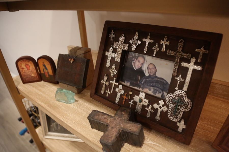 A photo of Anthoula Katsimatides' brothers John, left, and Michael Katsimatides, right, who died just one year apart from each other, sits on a shelf beside a cross fashioned from the steel of the fallen World Trade Center on Monday, Aug. 30, 2021, in the Queens borough of New York. John often visited the old St. Nicholas Greek Orthodox Church to say a prayer and light a candle as he went to or from work nearby on the 104th floor of the World Trade Center's north tower. The church stood as a quiet oasis amid the soaring financial district.