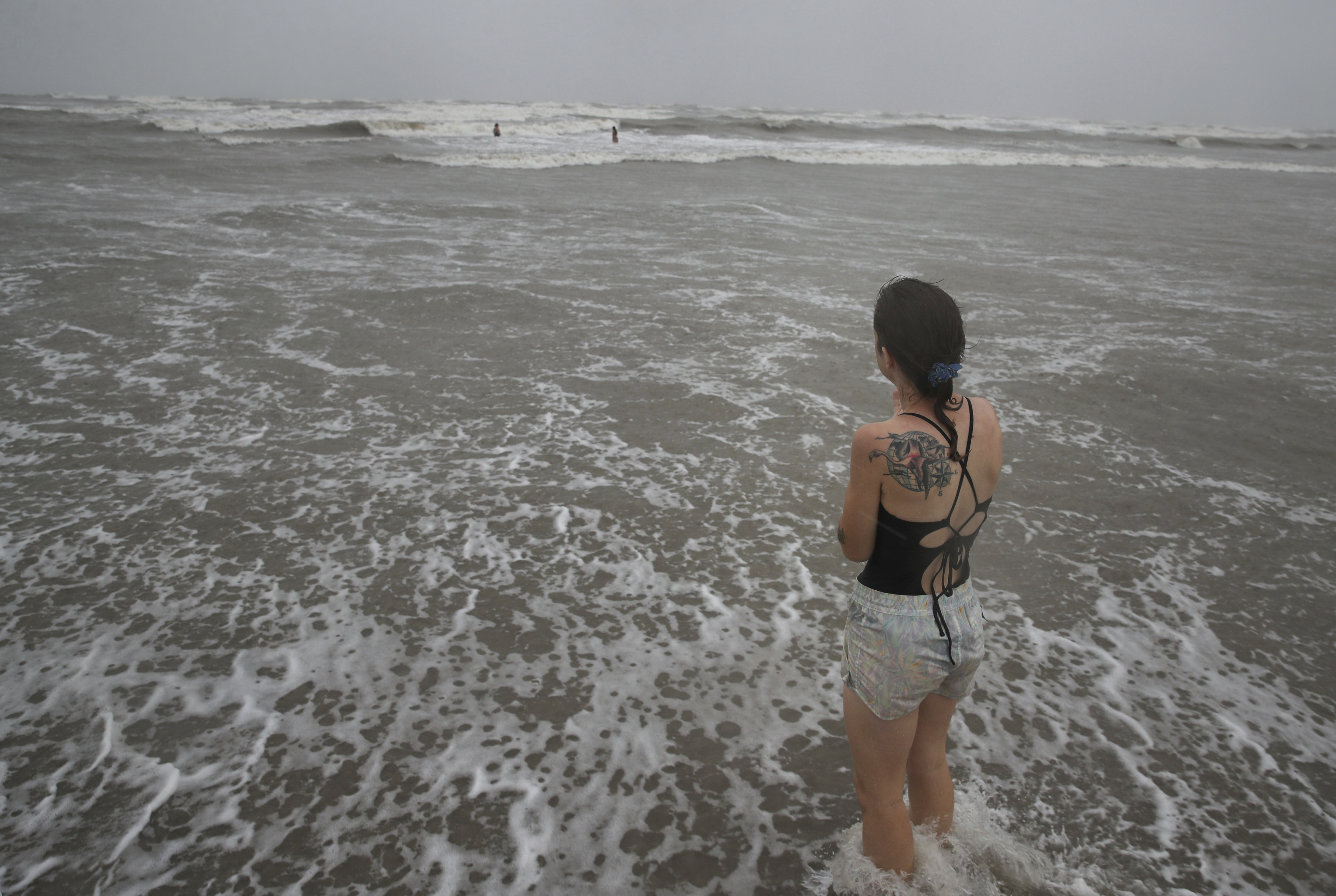 A woman watches her friends swim as Tropical Storm Nicholas approaches the Texas coast