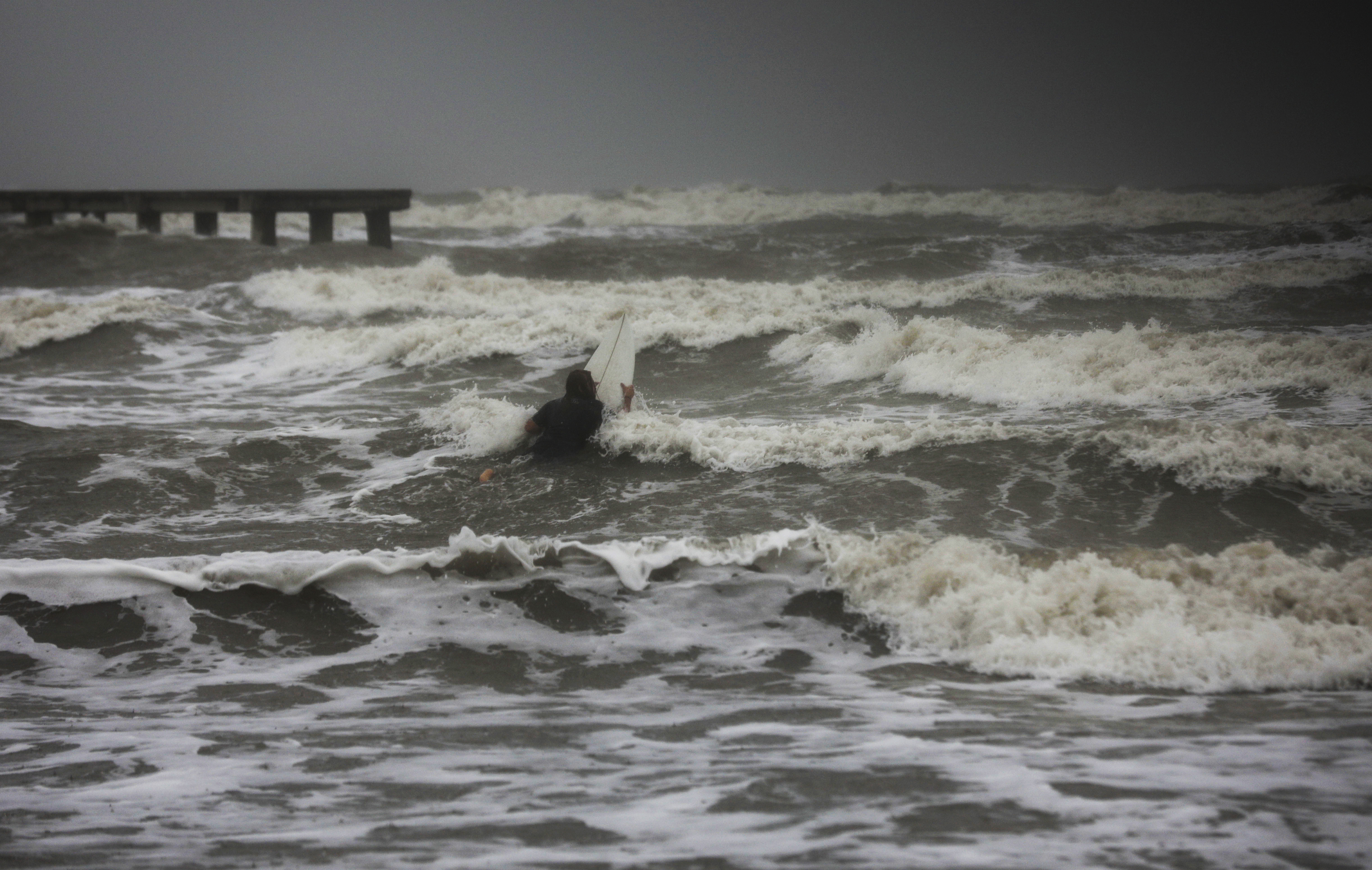 A surfer tries to paddle through the surf as wind and rain from Tropical Storm Nicholas batters the area