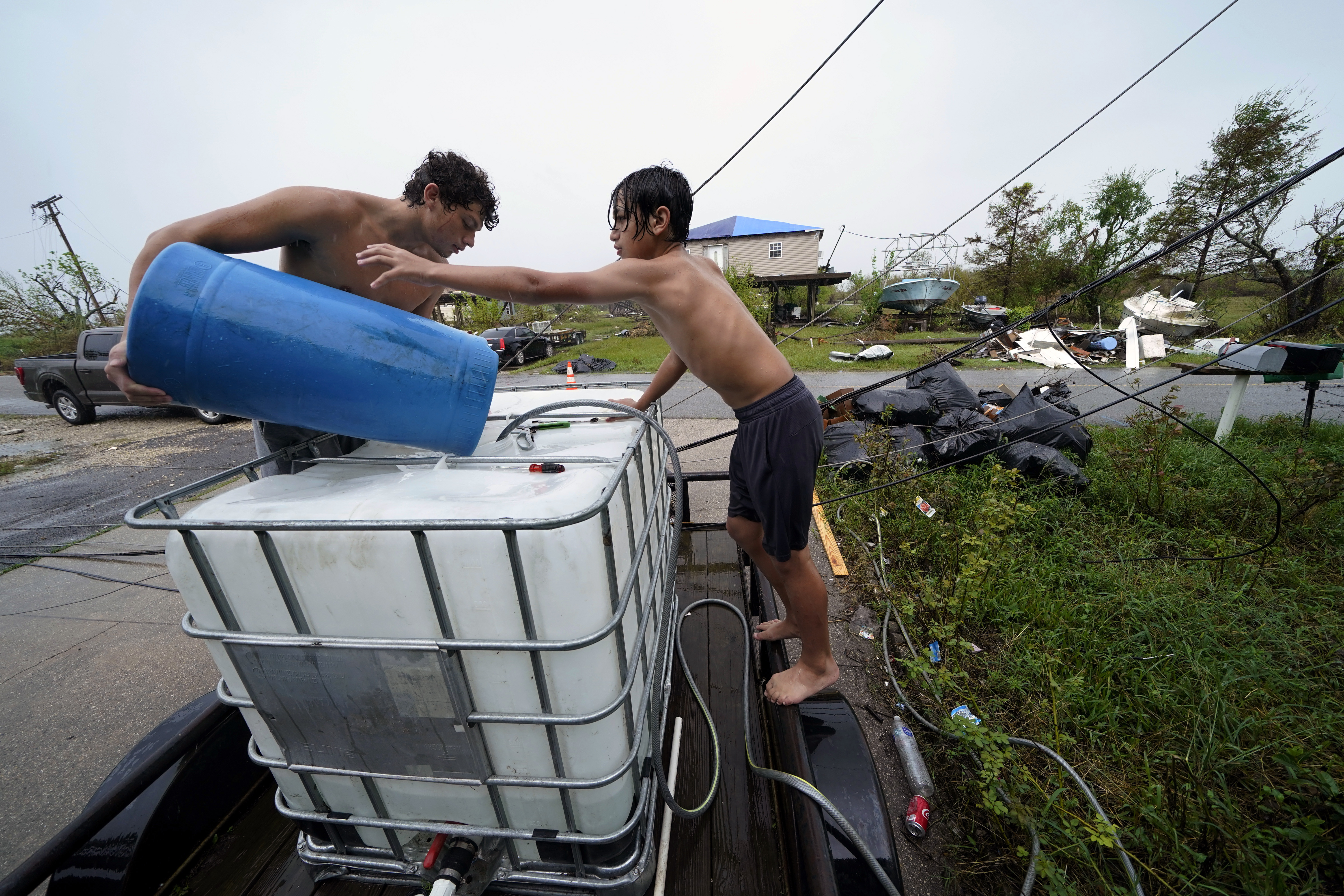 Terren Dardar, 17, and Dayton Verdin, 14, left, pour barrels of rainwater they collected from Tropical Storm Nicholas