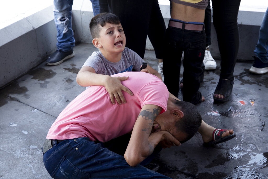 In this May 20, 2021, file photo, a boy screams for help after his father was injured when he was hit in the eye by a stone thrown by members of the Christian rightwing Lebanese Forces group, who attacked buses carrying Syrian voters, in the town of Zouk Mosbeh, north of Beirut, Lebanon. Mobs of angry Lebanese men attacked buses and cars carrying Syrians expatriates and others heading to the Syrian embassy in Beirut protesting against what they said was an organized vote for President Bashar Assad.