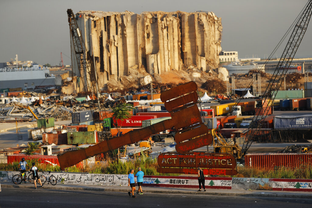 In this Aug. 4, 2021, file photo, people pass next of a justice symbol monument that sits in front of towering grain silos gutted in the massive August 2020 explosion at the Beirut port that claimed the lives of more than 200 people, in Beirut, Lebanon. Countries like Lebanon, Syria, Iraq, Lebanon and Yemen are all teetering on the brink of humanitarian catastrophe with an economic implosion that threatens to throw the region into even deeper turmoil.