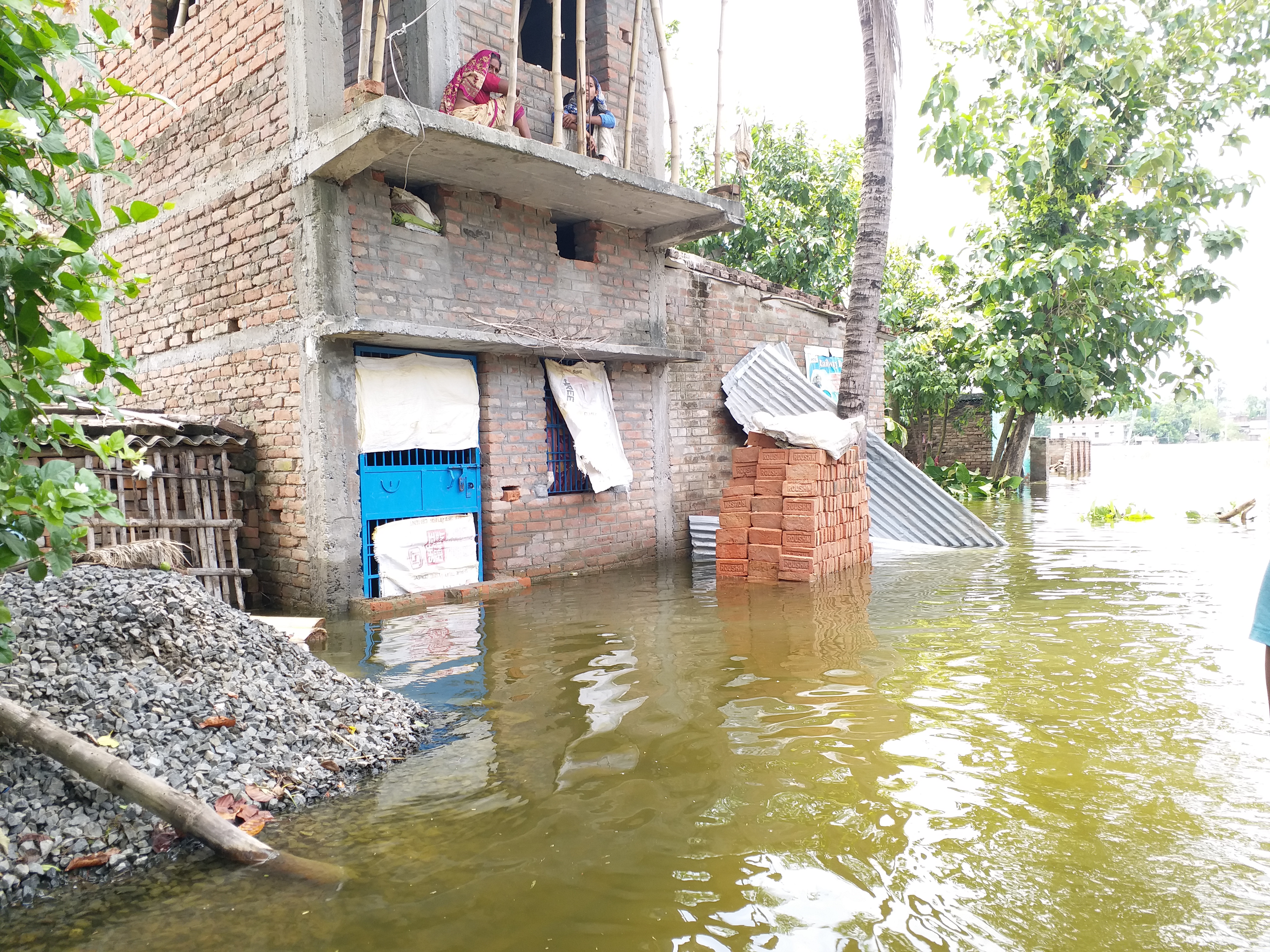 बाढ़ में घर की छत पर बैठ बाहर का नजारा देखती दो महिला