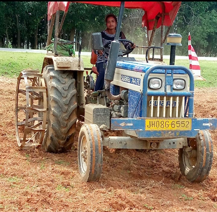 girl driving tractor in field in Gumla
