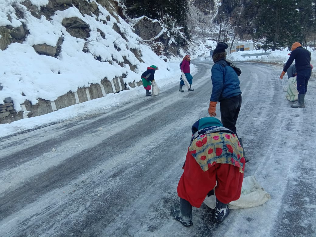 सड़क पर फिसलन को कम करने के लिए यूरिया और नमक डालते हुए लोग.