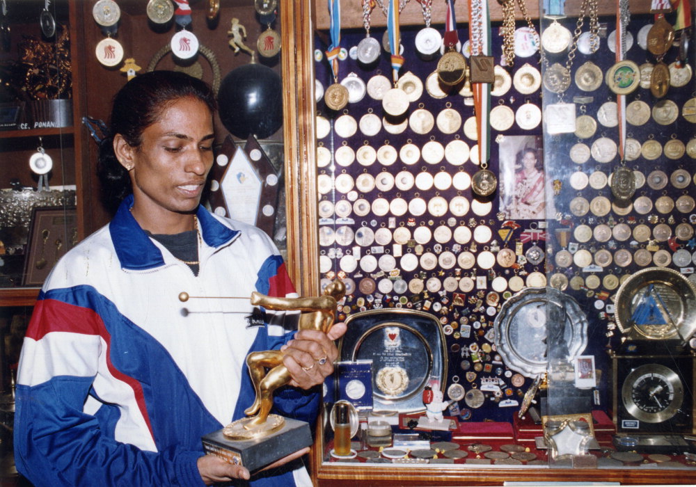 PT Usha poses for a photo in front of medals.