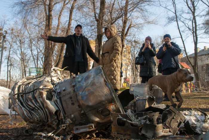 People stand next to fragments of military equipment on the street in the aftermath of an apparent Russian strike in Kharkiv in Kharkiv, Ukraine, Thursday, Feb. 24, 2022. Russian troops have launched their anticipated attack on Ukraine. Big explosions were heard before dawn in Kyiv, Kharkiv and Odesa as world leaders decried the start of an Russian invasion that could cause massive casualties and topple Ukraine's democratically elected government.